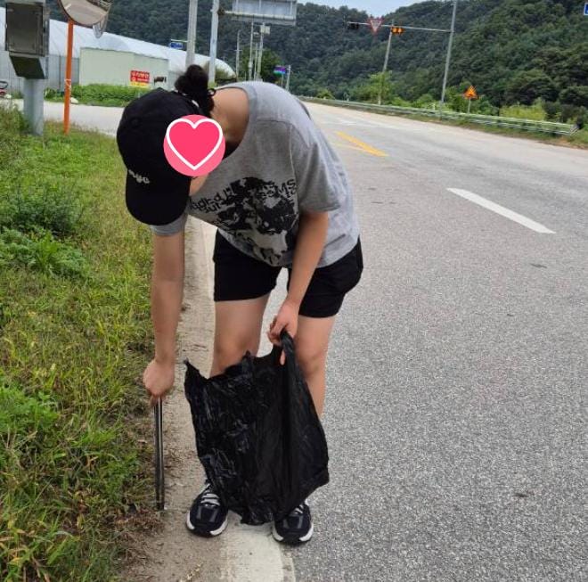 국도 갓길에서 허리를 굽혀 봉투에 쓰레기를 담는 모습