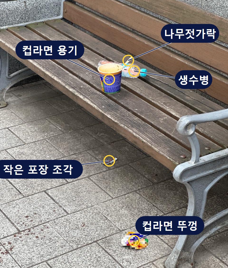 벤치 위에 컵라면 용기, 생수병, 나무젓가락, 바닥에 컵라면 뚜껑과 작은 포장 조각이 남아 있는 사진