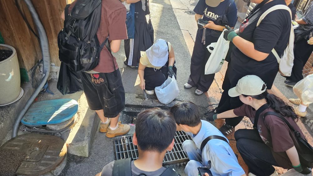 배수구 앞에 둘러앉아 함께 살펴보며 기록하는 청소년들